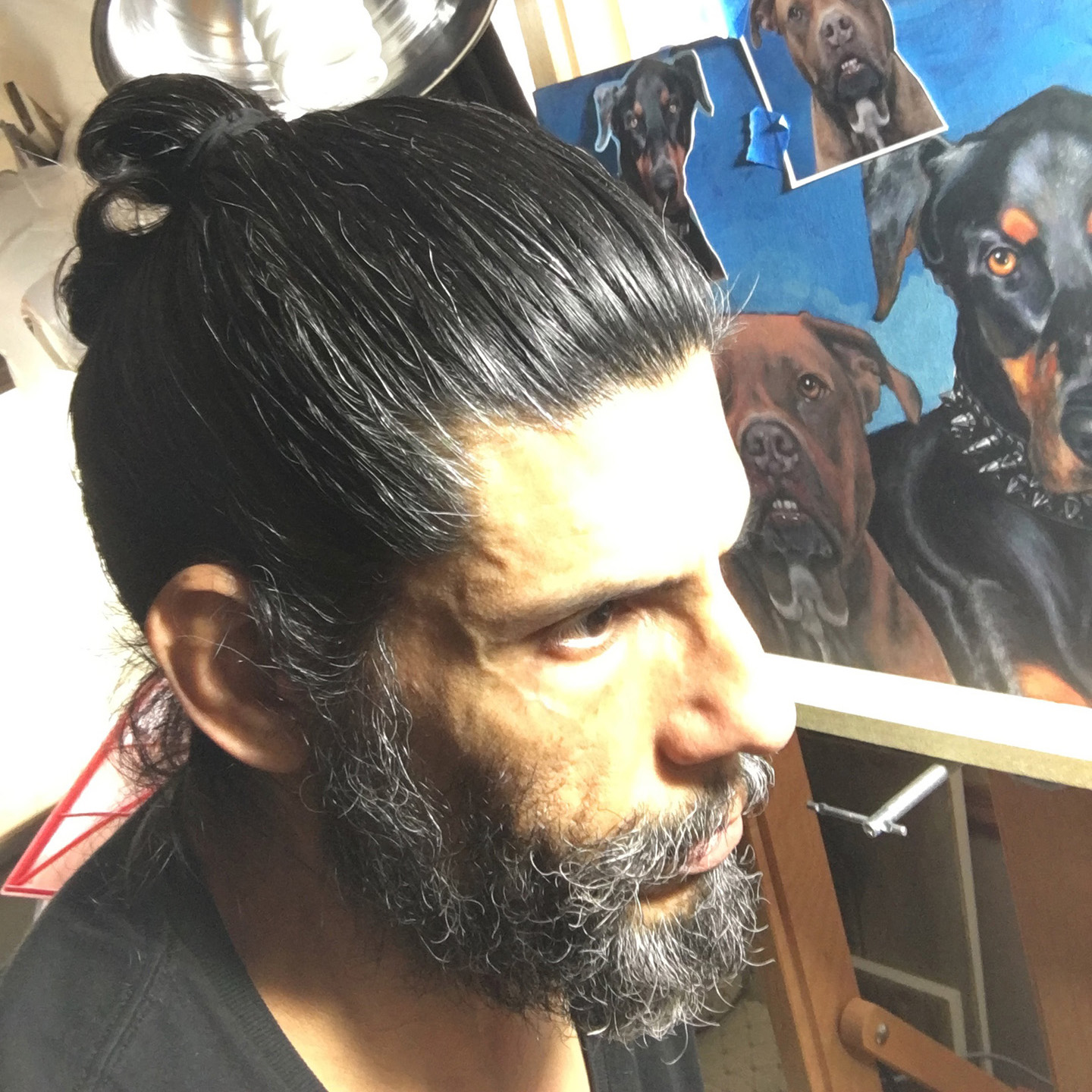Portrait of artist Carlos J. Flores in his studio, with a painting of two dogs in the background.